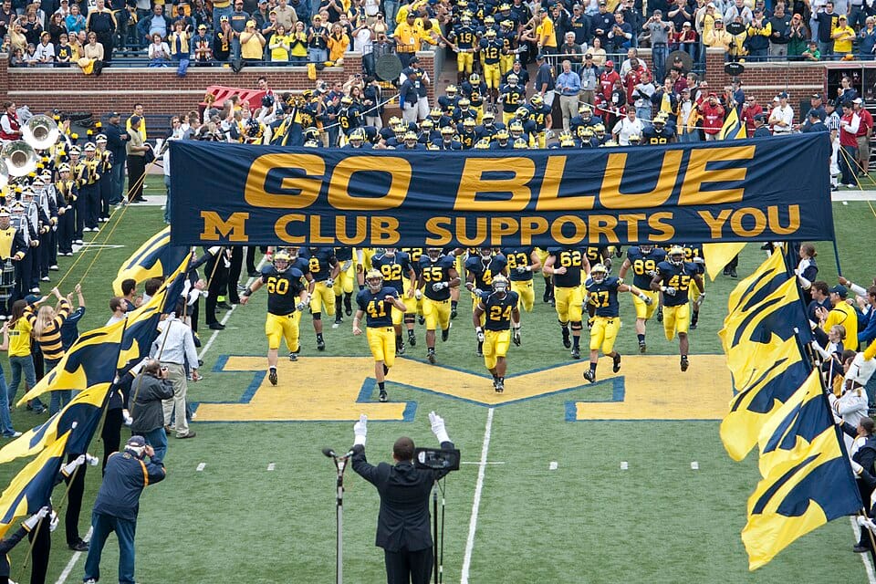 University of Michigan Wolverines football team entering the field as the marching band salutes.